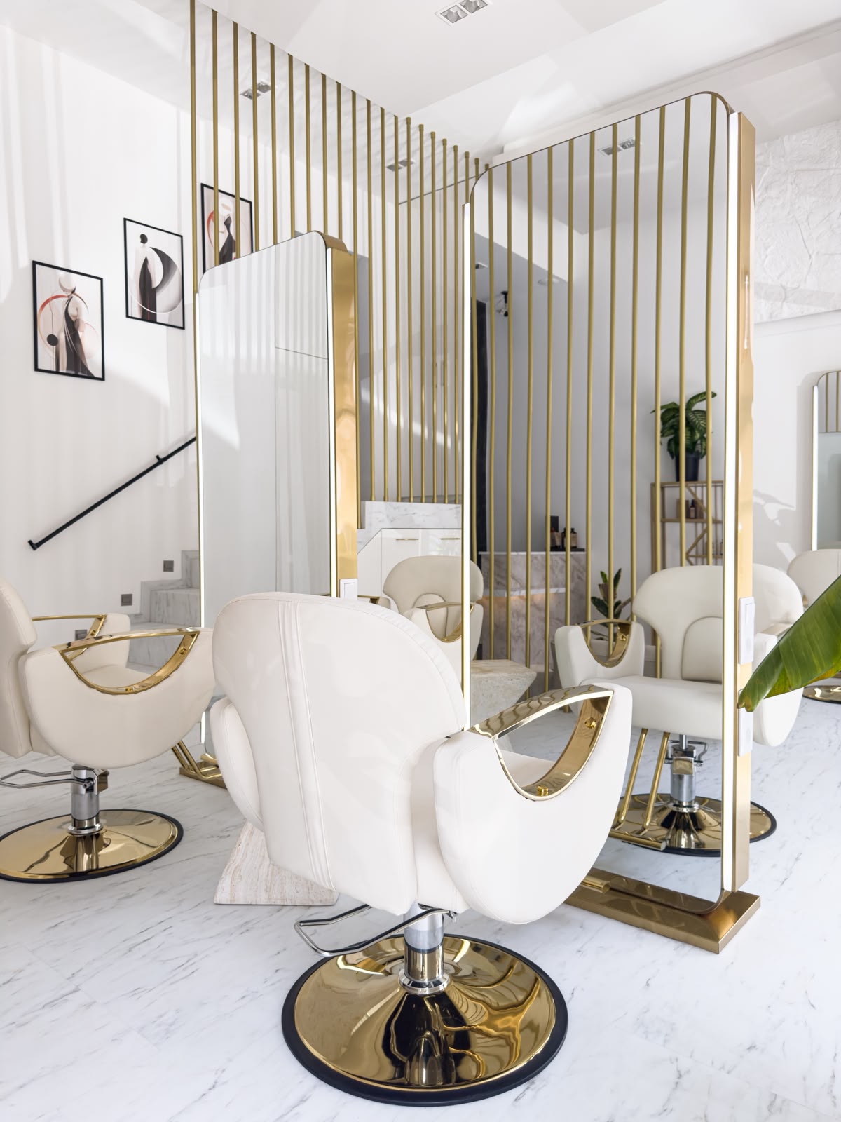Wnętrze salonu Wojnar Art Hair — białe fotele ze złotymi detalami, złote przepierzenia i marmurowe schody